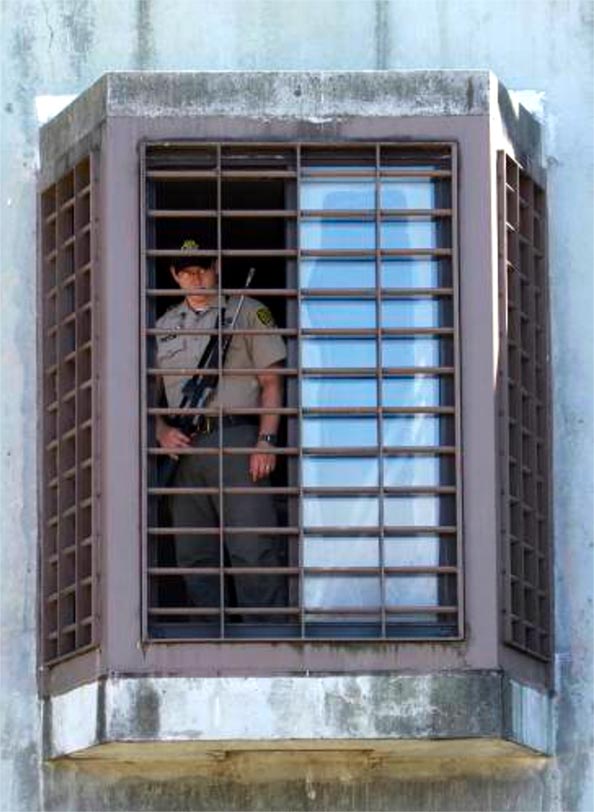 Correctional officer with weapon looking out barred window from a prison